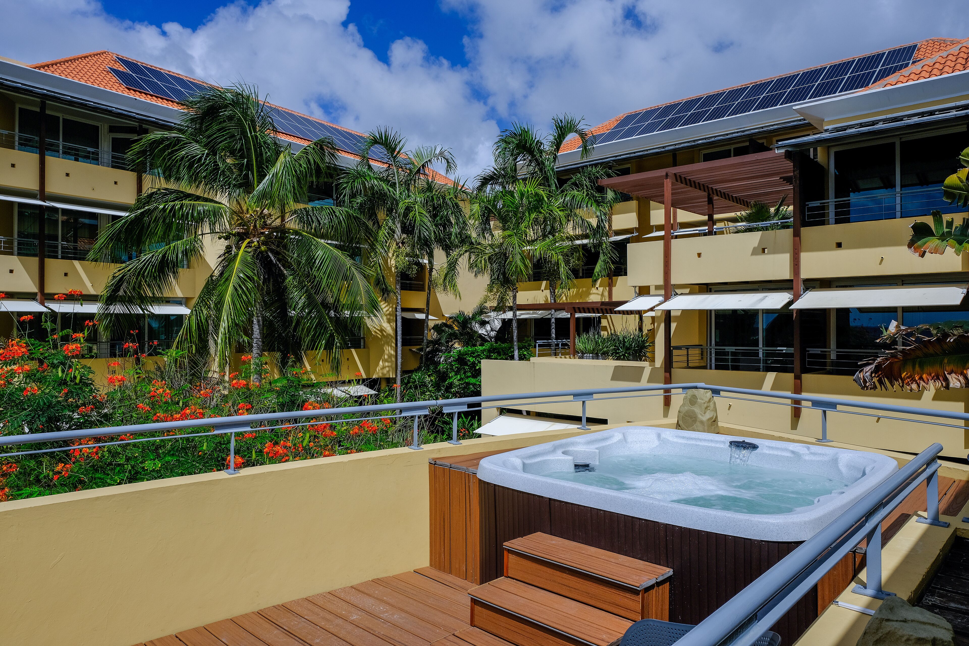 A rooftop deck with a hot tub, palm trees, and solar panels on the building.