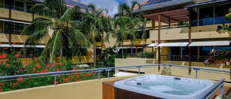 A rooftop deck with a hot tub, palm trees, and solar panels on the building.