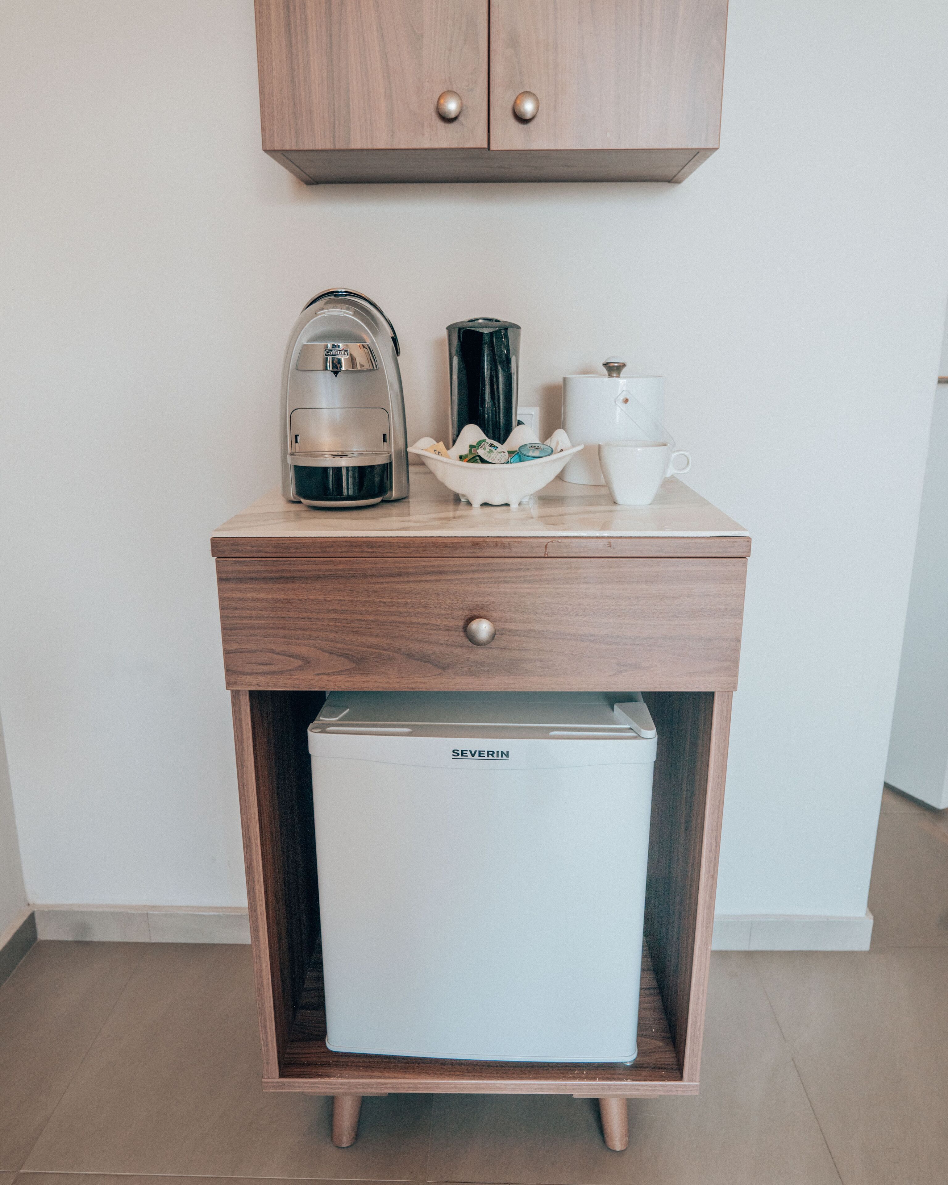 Un angolo cottura compatto con macchina da caffè, teiera e piccolo frigorifero.