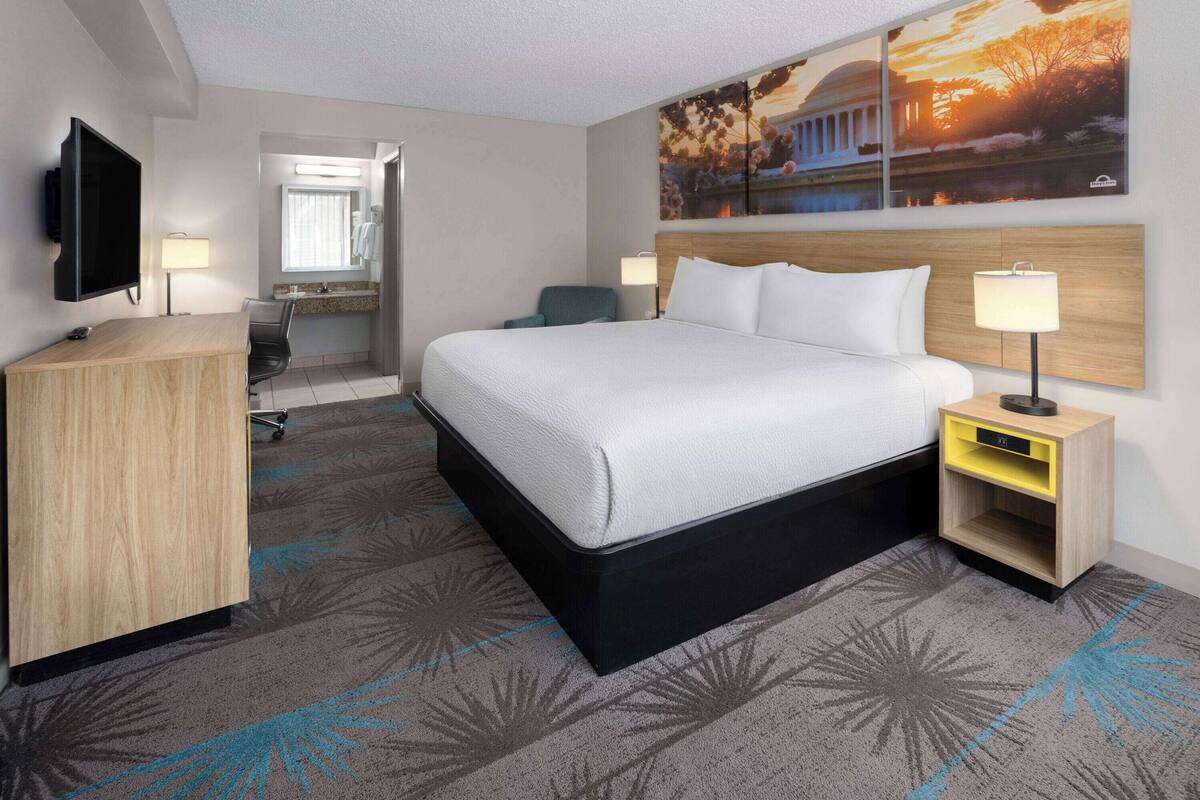 Ein Hotelzimmer mit einem großen Bett, einem Schreibtisch, einem Fernseher und einem Gemälde an der Wand.