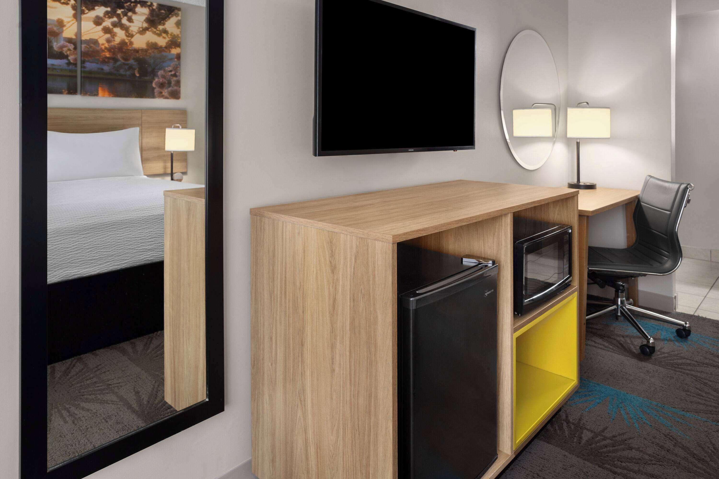 A hotel room with a bed, a desk with a computer, a TV, a mirror, and a chair.