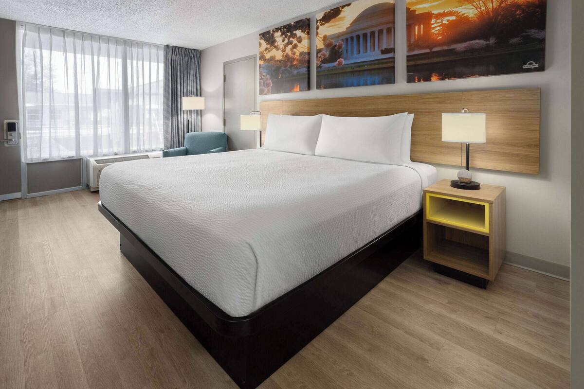 Ein Hotelzimmer mit einem großen Bett, einem Nachttisch mit Lampe, einem Sessel und einem Fenster mit Vorhängen.