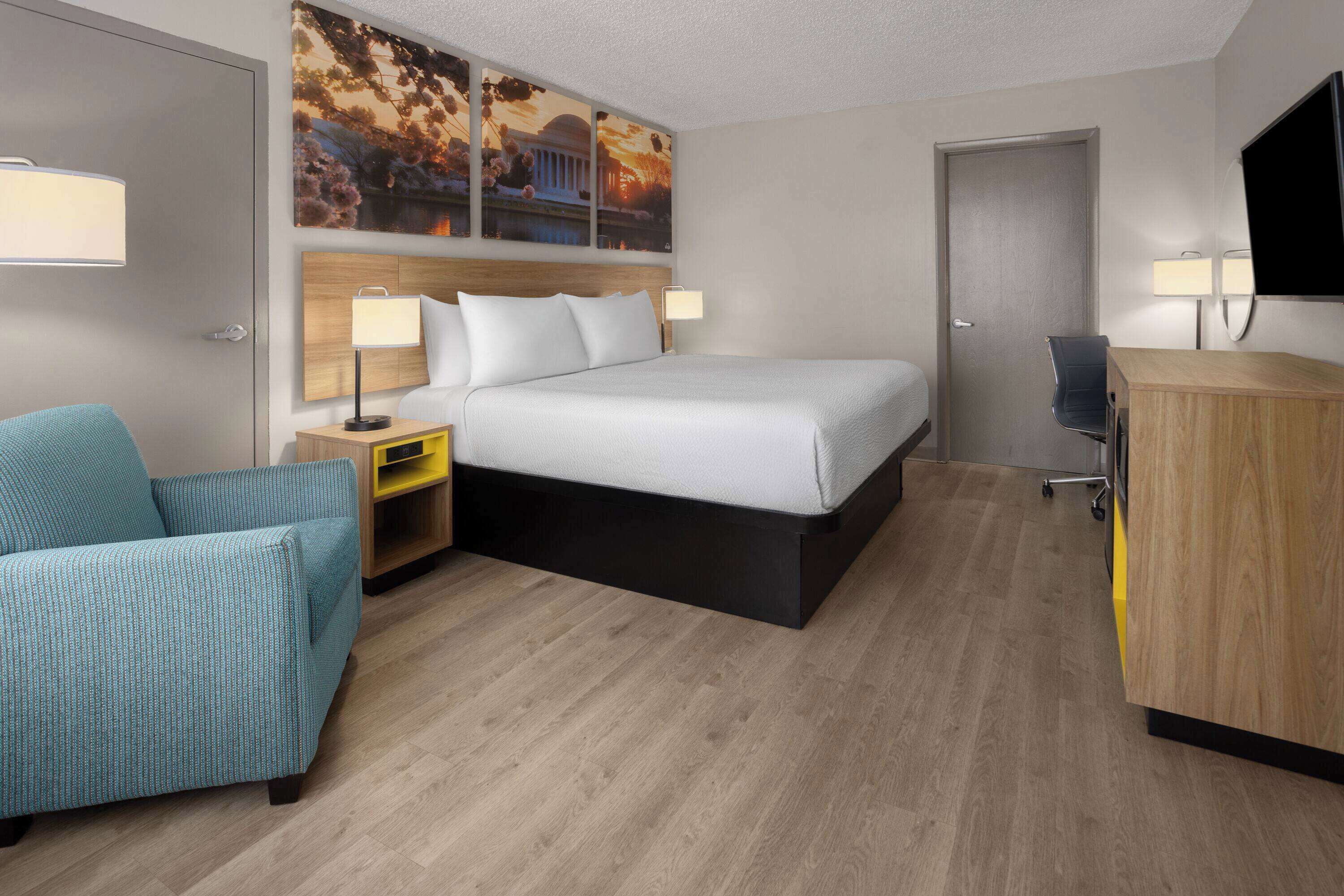 Ein Hotelzimmer mit Bett, Schreibtisch, Sessel, Fernseher und Bildern an der Wand.