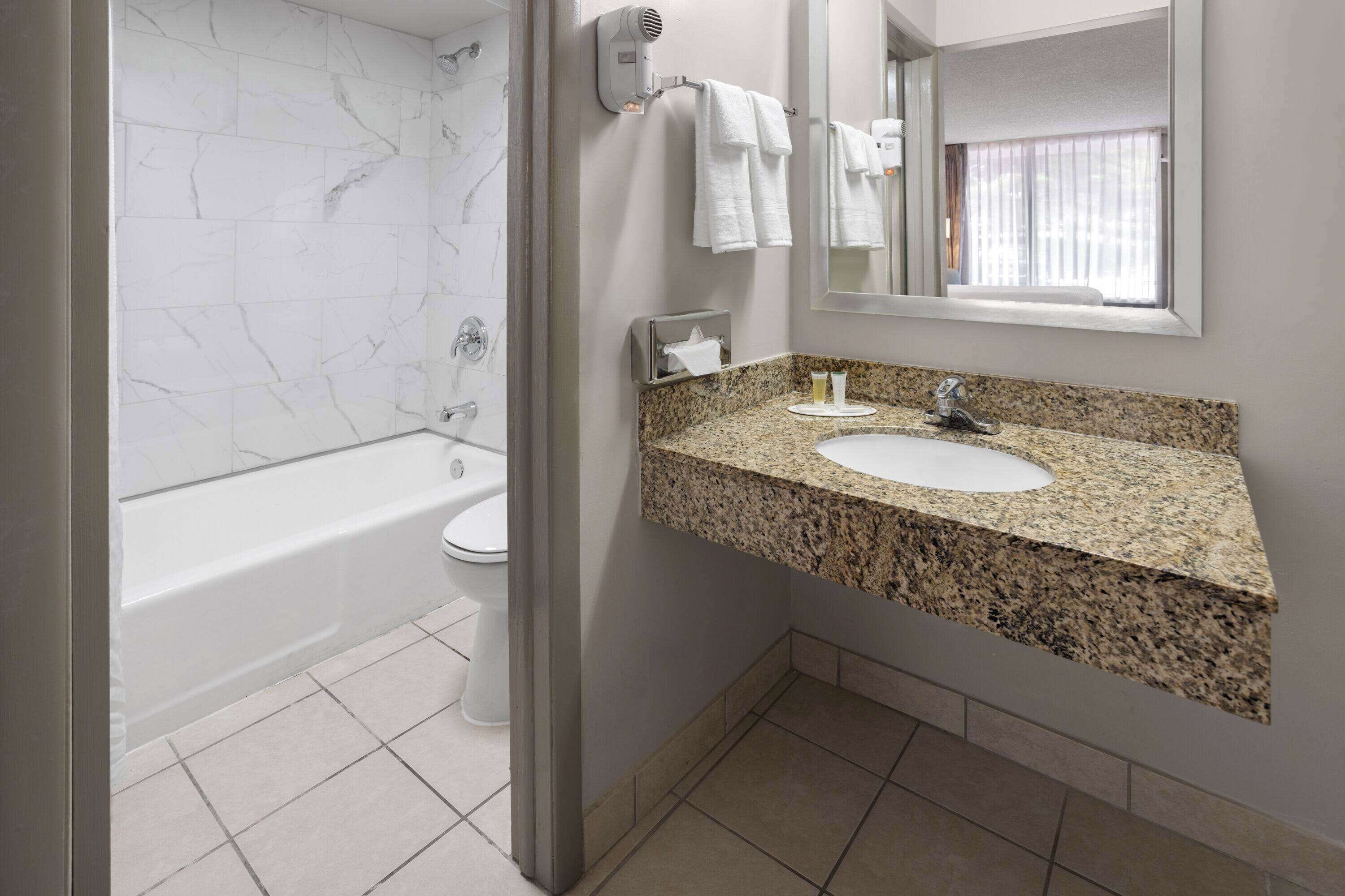 A modern bathroom with a marble wall, a freestanding bathtub, a granite countertop sink, and a mirror above the sink.