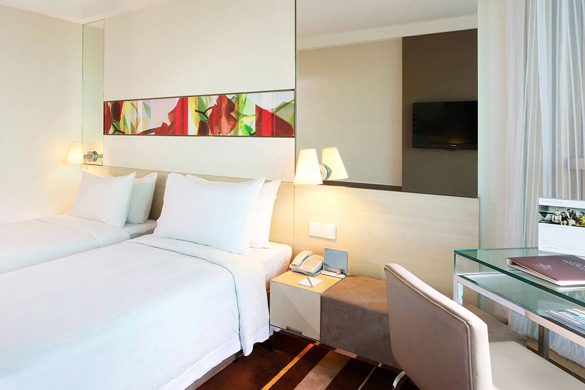 A hotel room with two beds, a desk, a chair, a telephone, and a television.
