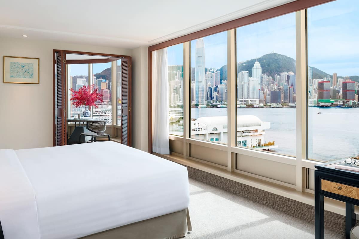 A hotel room with a large bed, a desk, and a view of a city skyline and water.
