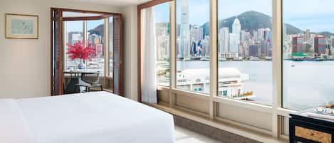 A hotel room with a large bed, a desk, and a view of a city skyline and water.