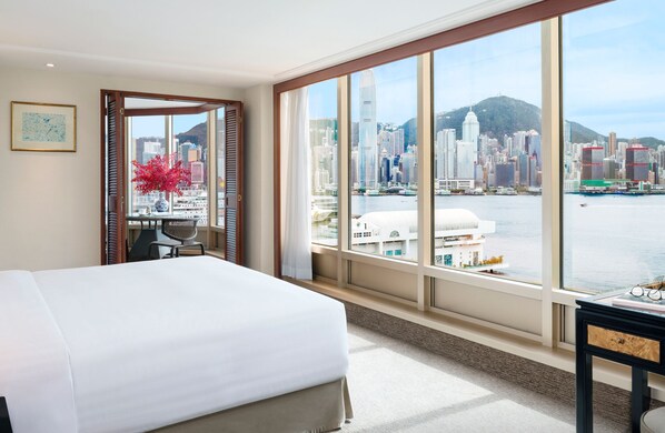 Habitación de hotel con una cama grande, un escritorio y vistas a un horizonte urbano y al agua.