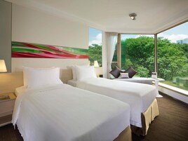 Habitación de hotel con dos camas, un ventanal con vistas a la vegetación y un cuadro abstracto de colores en la pared.
