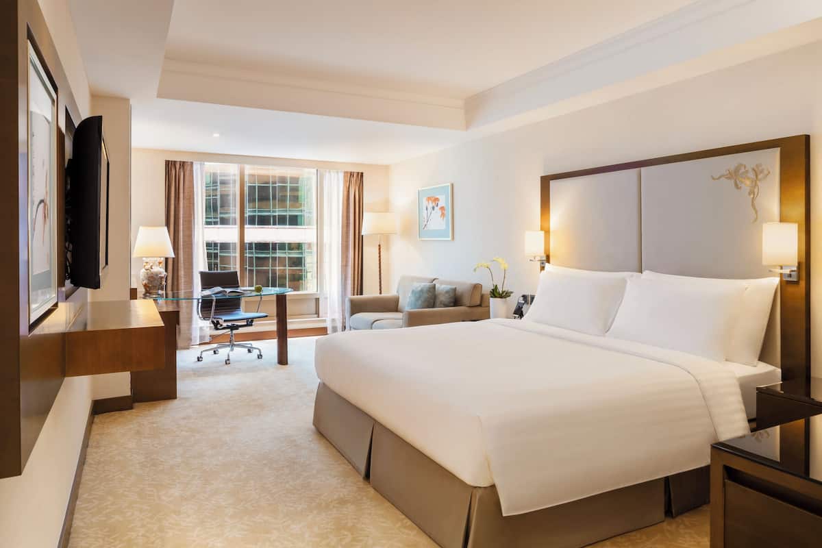 A hotel room with a large bed, a desk with a chair, a sofa, and a TV on the wall.