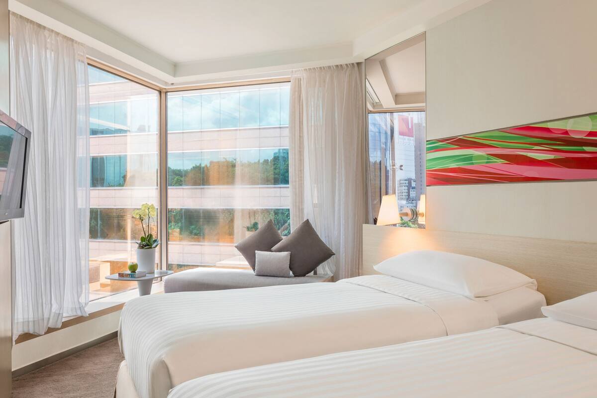 A hotel room with two beds, a large window with curtains, a flat-screen TV, and a colorful abstract painting on the wall.