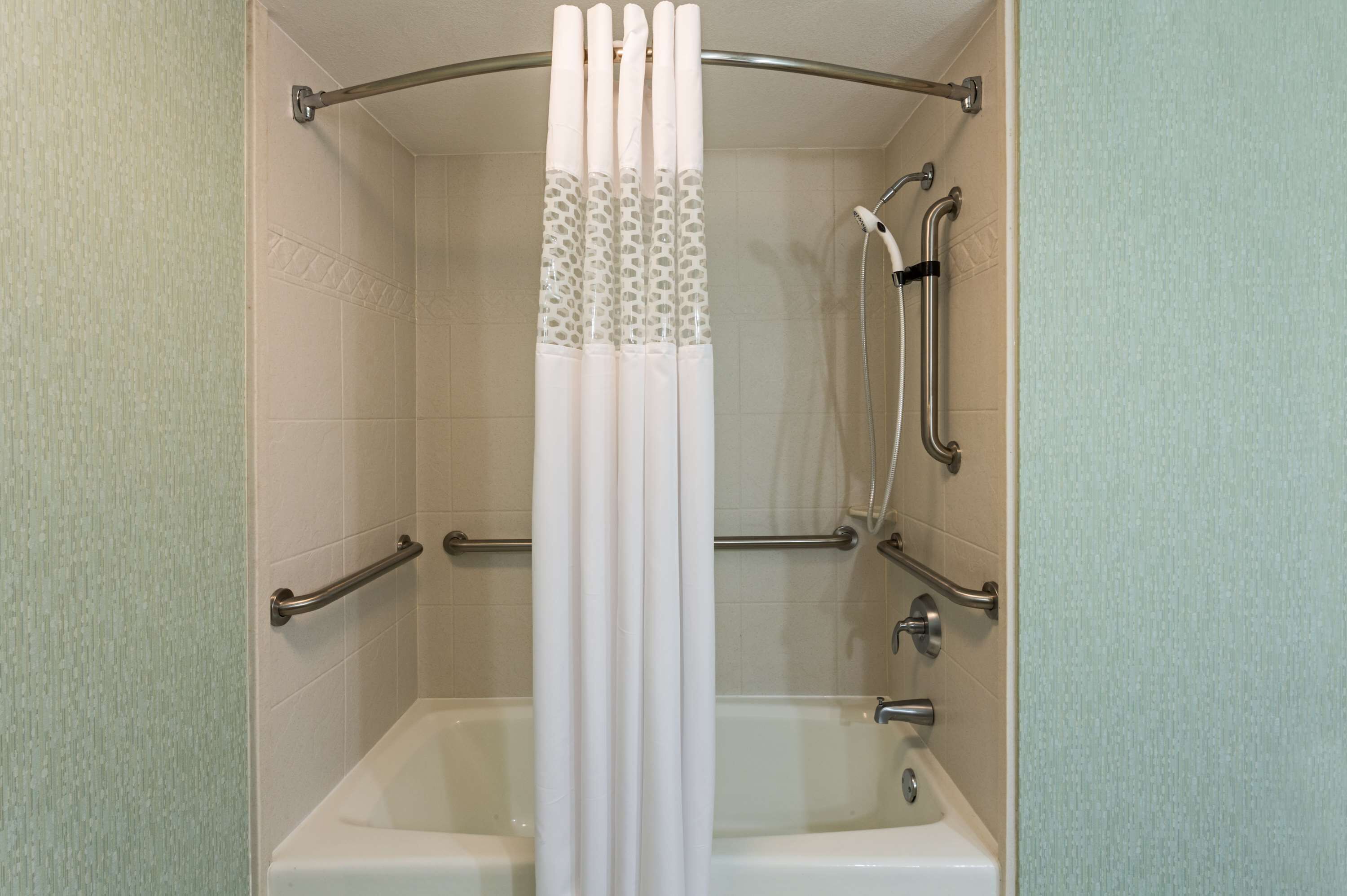 Ein Duschbereich mit Badewanne, Haltegriffen und Duschkopf.