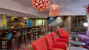 A hotel lobby with a long reception desk, multiple seating areas with red and purple chairs, and large decorative spherical light fixtures.
