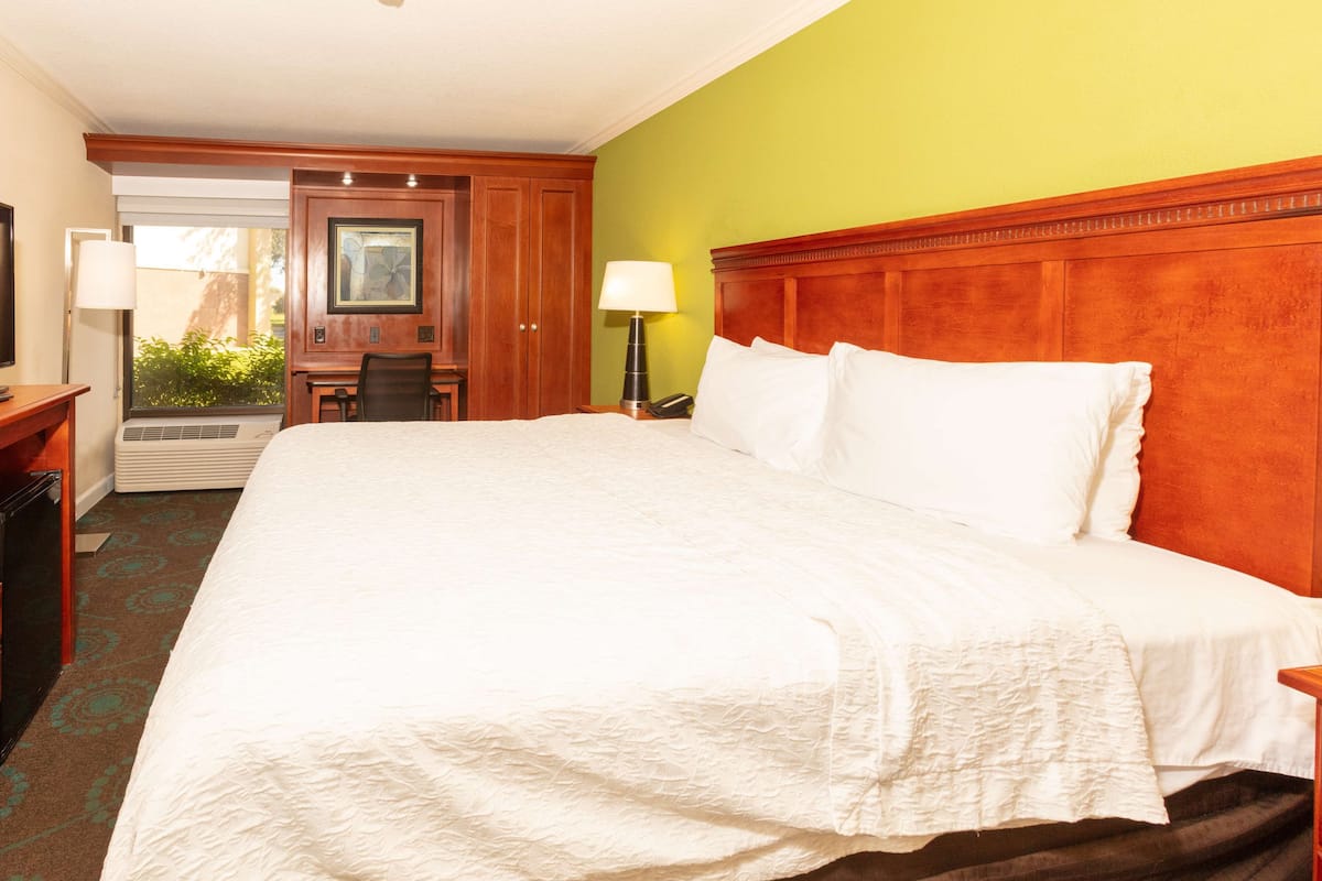 A hotel room with a large bed, a desk with a chair, a lamp, and a telephone.
