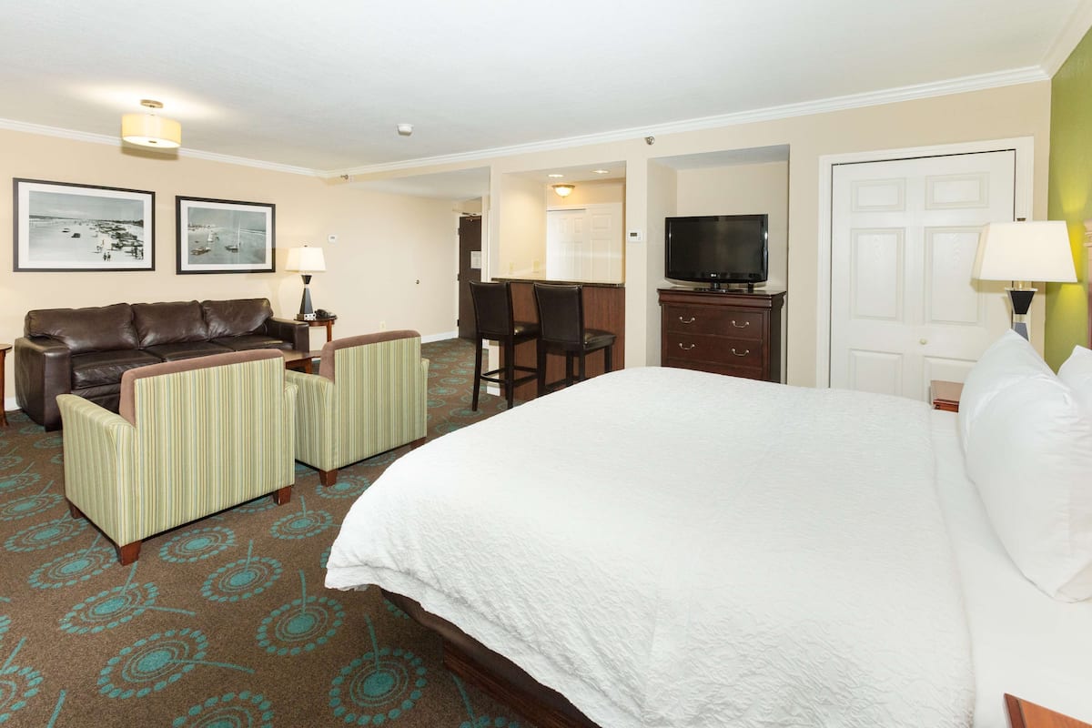 A hotel room with a large bed, a leather sofa, two armchairs, a television, and a desk.