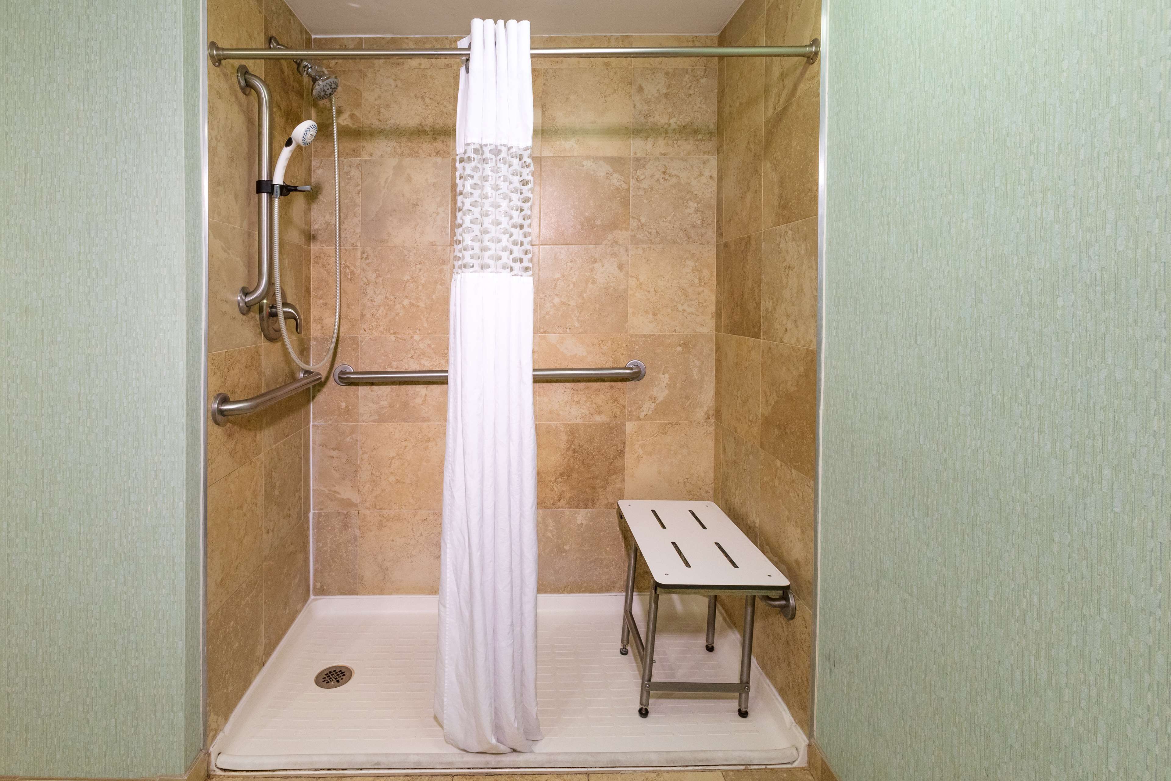 A walk-in shower with a white shower curtain, grab bars, and a small step stool.
