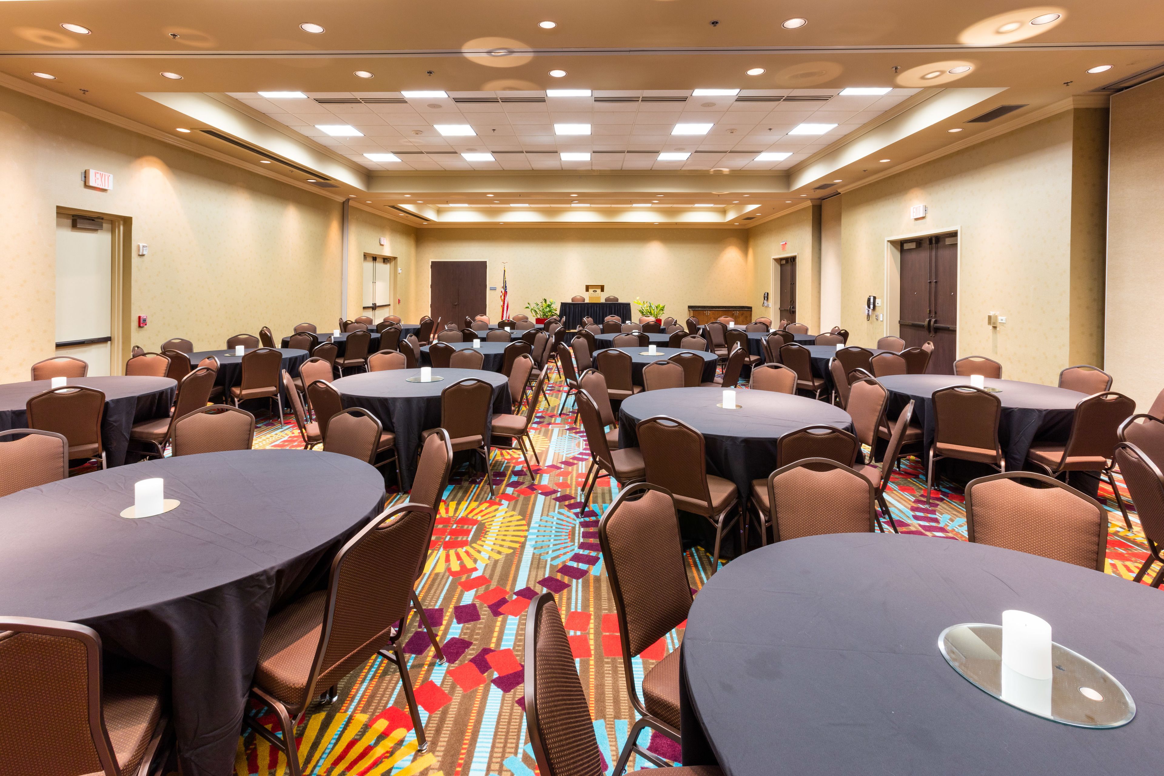 A conference room with multiple round tables, chairs, and a carpeted floor.