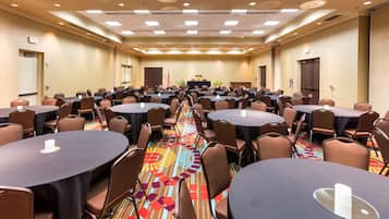 Un salón de conferencias con varias mesas redondas, sillas y suelo alfombrado.