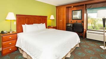 Hotelkamer met een groot bed, een houten hoofdbord, twee nachtkastjes met lampen, een bureau met stoel, en een raam met uitzicht op groen.