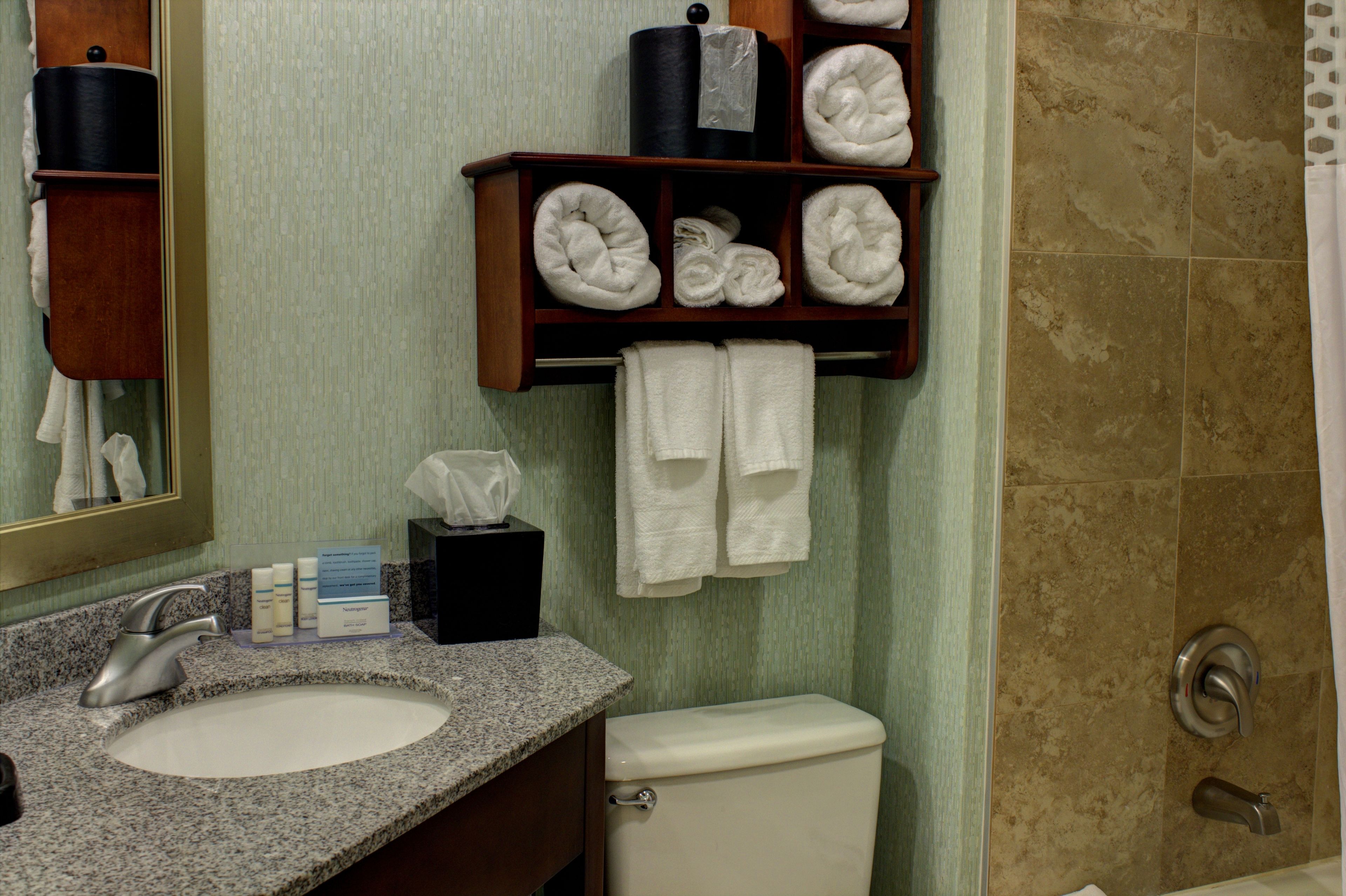 A bathroom with a granite sink, a toilet, a towel rack with neatly folded towels, and a shower area.