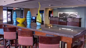 A hotel lobby with a reception desk, a large TV screen, and colorful vases on the counter.