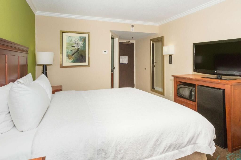 Quarto de hotel com cama, televisão, micro-ondas e porta que dá para outro cômodo.