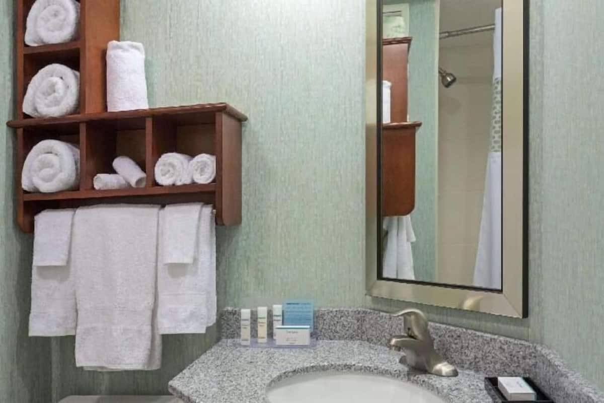 A bathroom with a sink, mirror, towel rack, and toiletries.