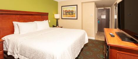 A hotel room with a large bed, a desk with a television, a nightstand, and a painting on the wall.