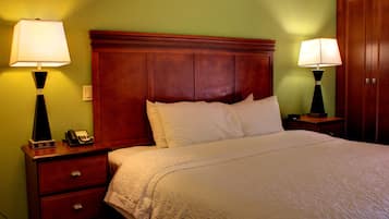 Habitación de hotel con una cama grande, dos mesitas de noche con lámparas, un cabecero de madera y un teléfono sobre una de las mesitas.