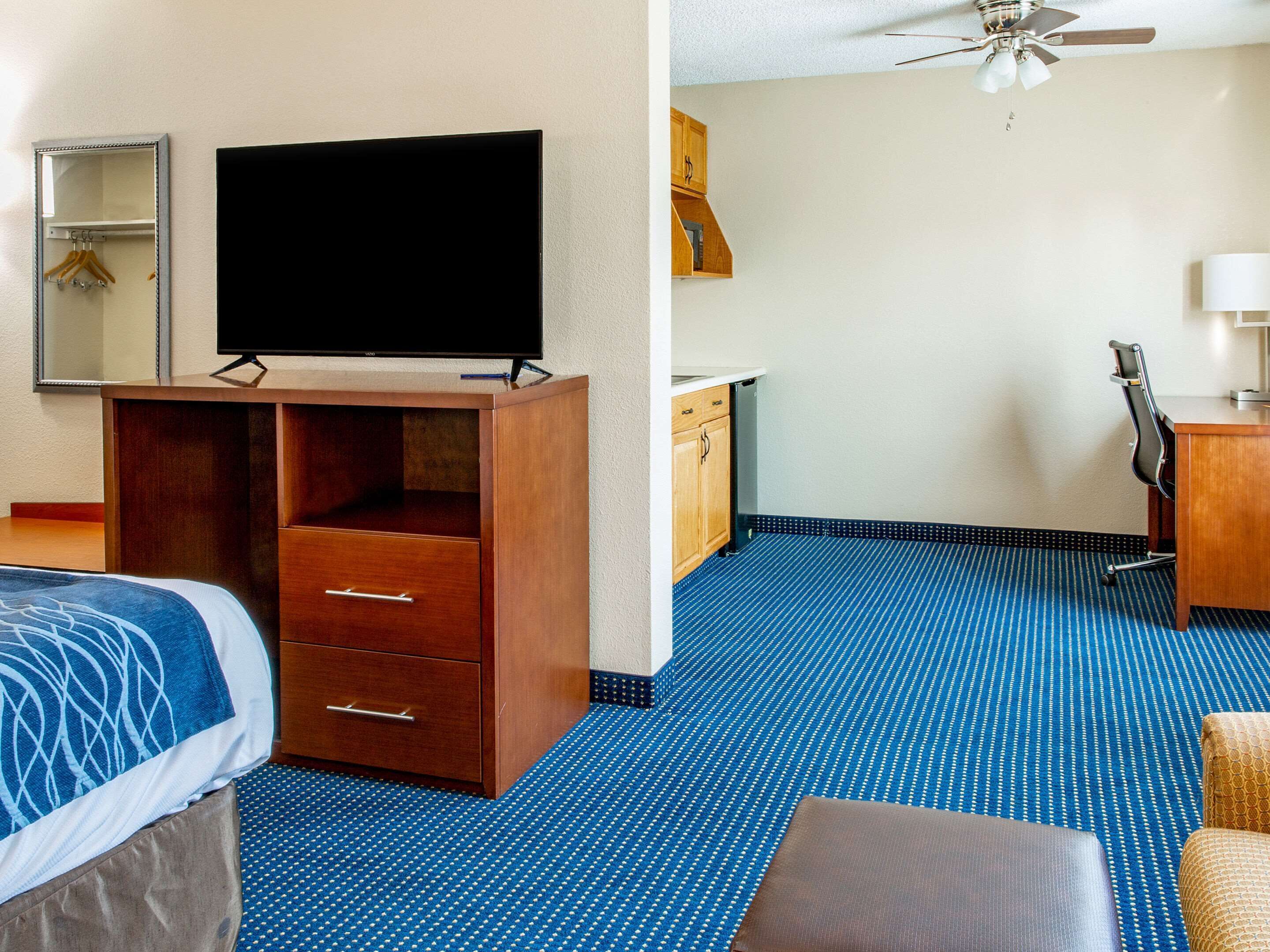 Une chambre d’hôtel équipée d’un lit, d’un bureau, d’une télévision, d’une armoire, d’un miroir et d’un ventilateur de plafond.