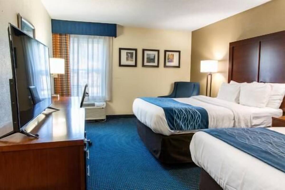 A hotel room with a bed, a desk with a computer, a chair, and a TV.