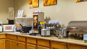 A breakfast bar with a waffle maker, coffee machine, and various condiments.