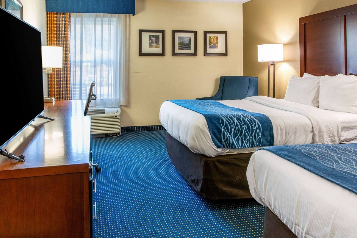 A hotel room with two beds, a desk with a television, a chair, and a window with curtains.