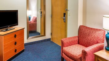 Quarto de hotel com cômoda de madeira, televisão, poltrona vermelha com padrão e tapete azul.