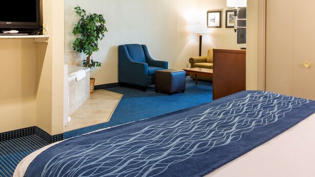 A hotel room with a bed, a blue armchair, a small table, a lamp, and a television on a stand.