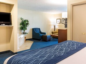 A hotel room with a bed, a blue armchair, a small table, a lamp, and a television on a stand.