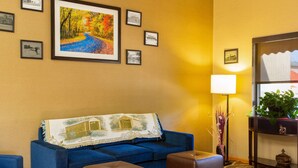 A hotel lobby with a blue sofa, two ottomans, a lamp, and framed pictures on the wall.