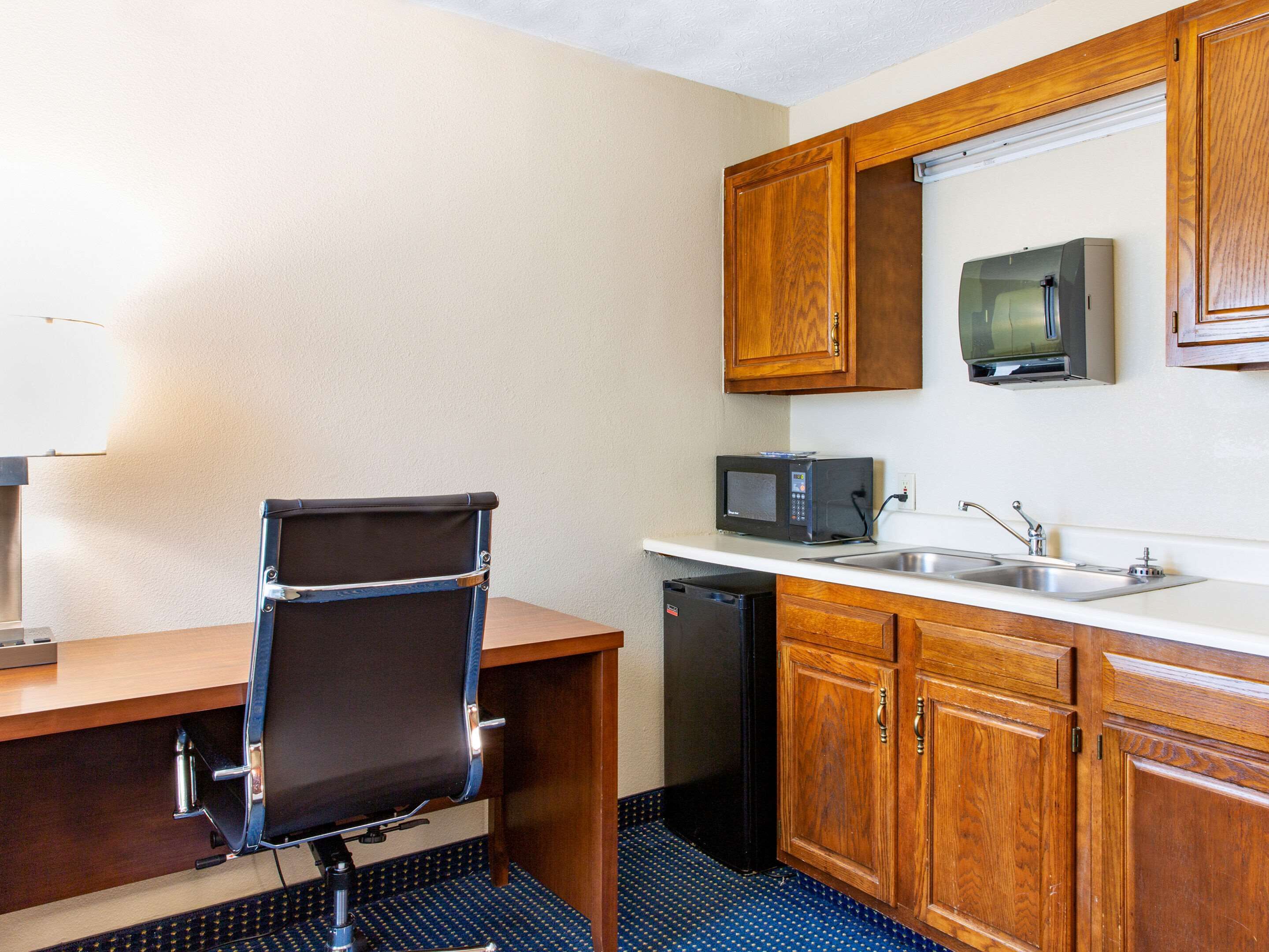 A compact kitchenette with a microwave, sink, and wooden cabinets.