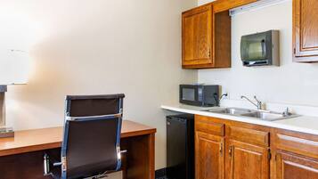 A compact kitchenette with a microwave, sink, and wooden cabinets.