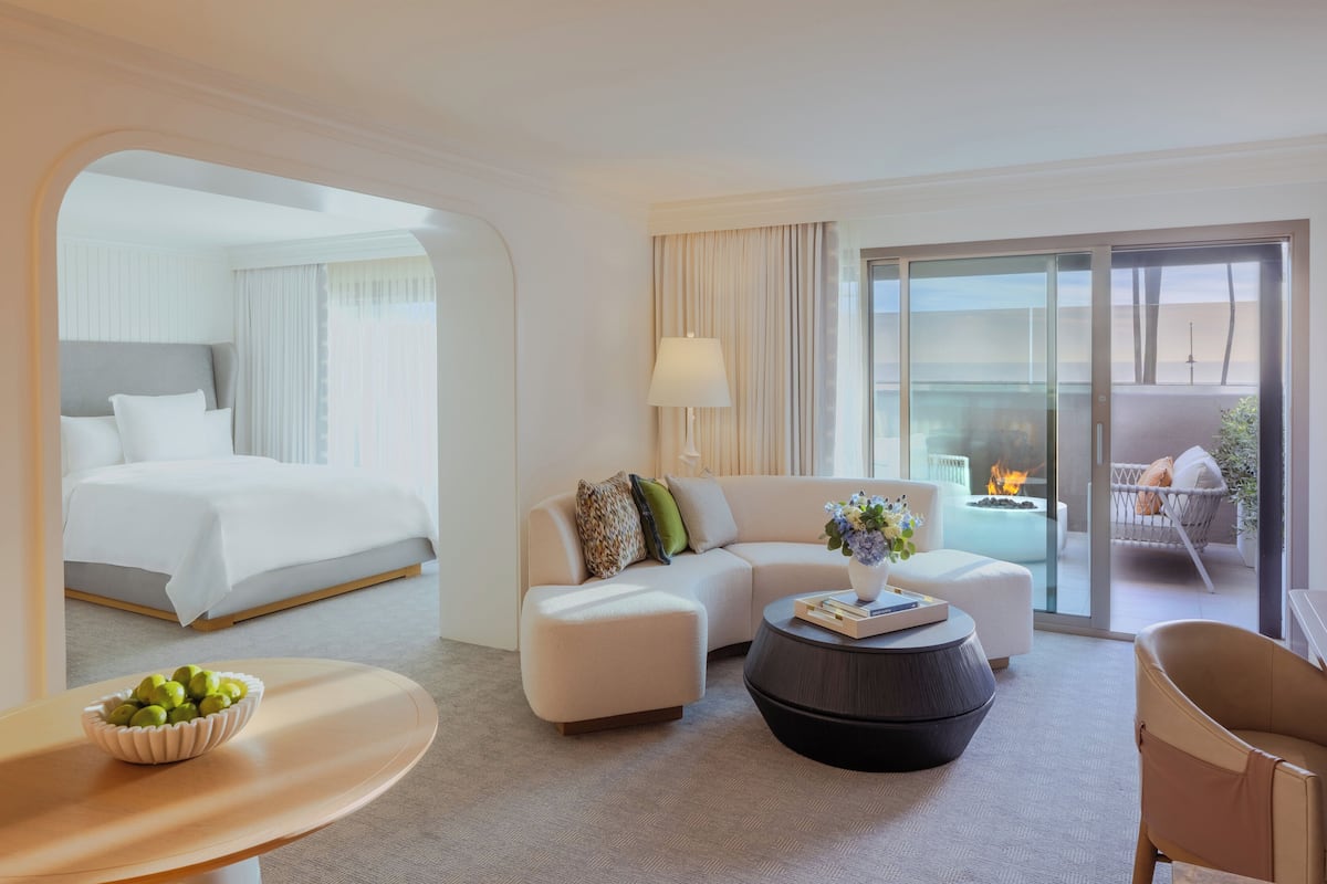 A hotel room with a bed, sofa, ottoman, coffee table, and a view of the outdoors.