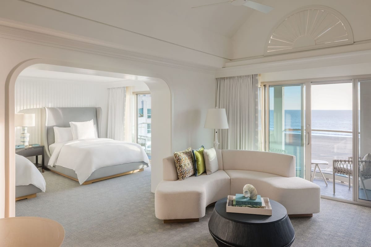 A hotel room with a bed, a sofa, a coffee table, and a balcony with a view of the sea.