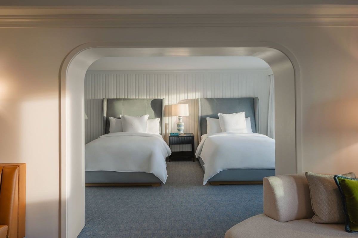 A hotel room with two beds, a nightstand, a lamp, and a sofa.