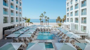 A poolside area with lounge chairs and umbrellas, overlooking a beach with palm trees. - Regent Santa Monica Beach by IHG (Santa Monica)