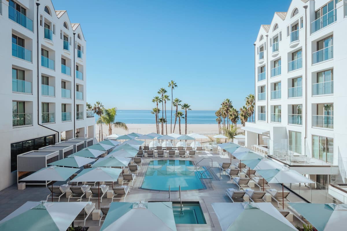 A poolside area with lounge chairs and umbrellas, overlooking a beach with palm trees.