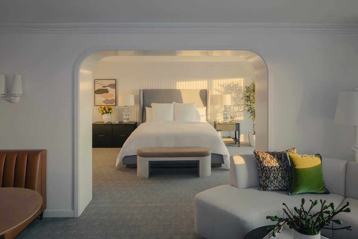 Una camera d'albergo moderna con un letto grande, una zona salotto con una panca e un tavolo da pranzo.