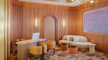 A modern interior with a wooden panel wall, a round table with chairs, a sofa, and a small side table with a drink.