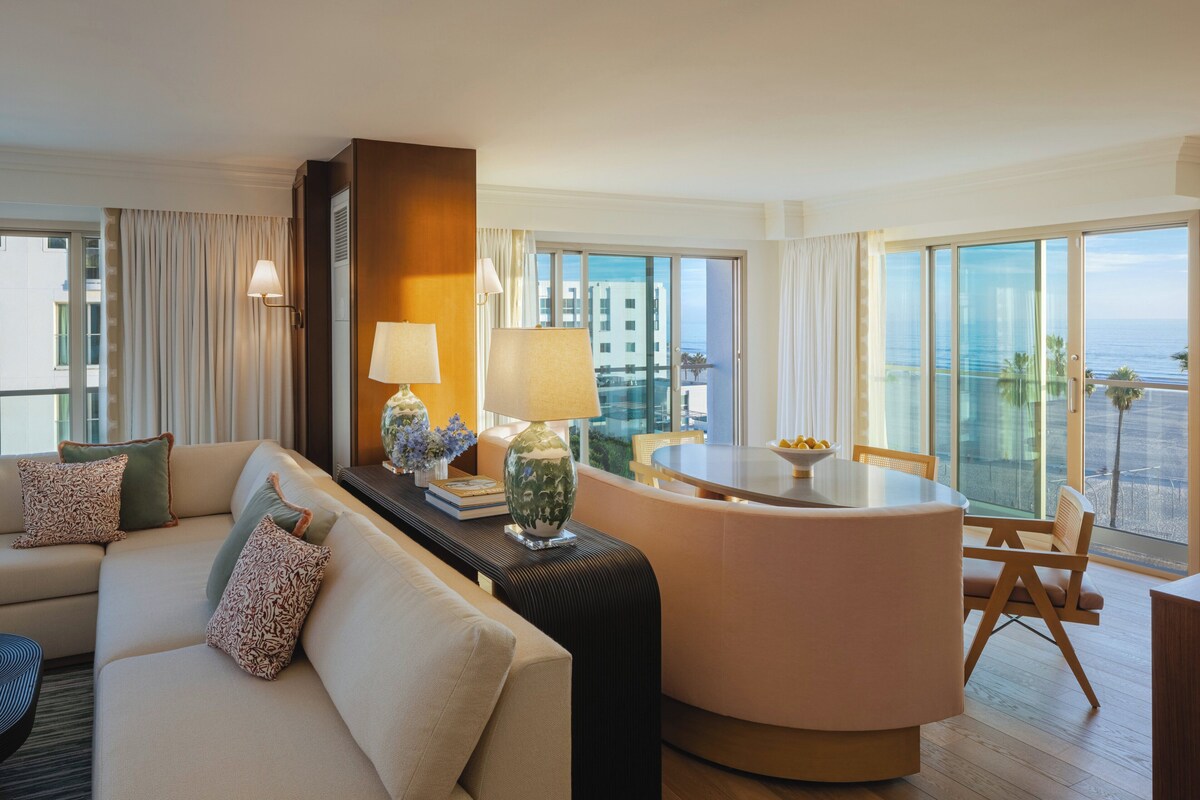A modern hotel room with a sofa, a dining table, and a view of the ocean.