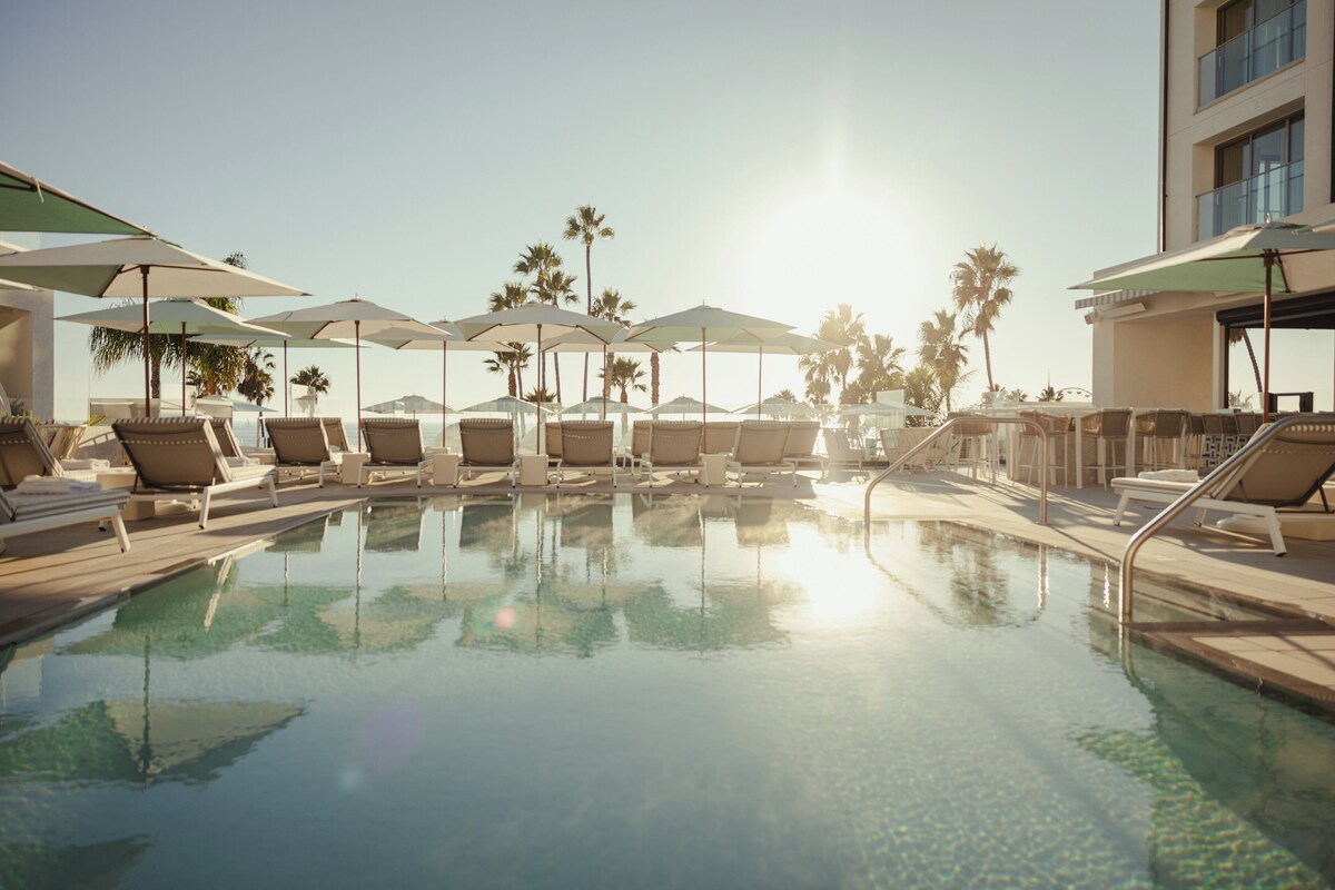A poolside area with lounge chairs and umbrellas, surrounded by palm trees.