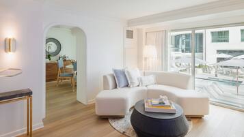 Una sala de estar moderna con un sofá blanco, una mesa redonda y vistas al área de la piscina a través de amplios ventanales.