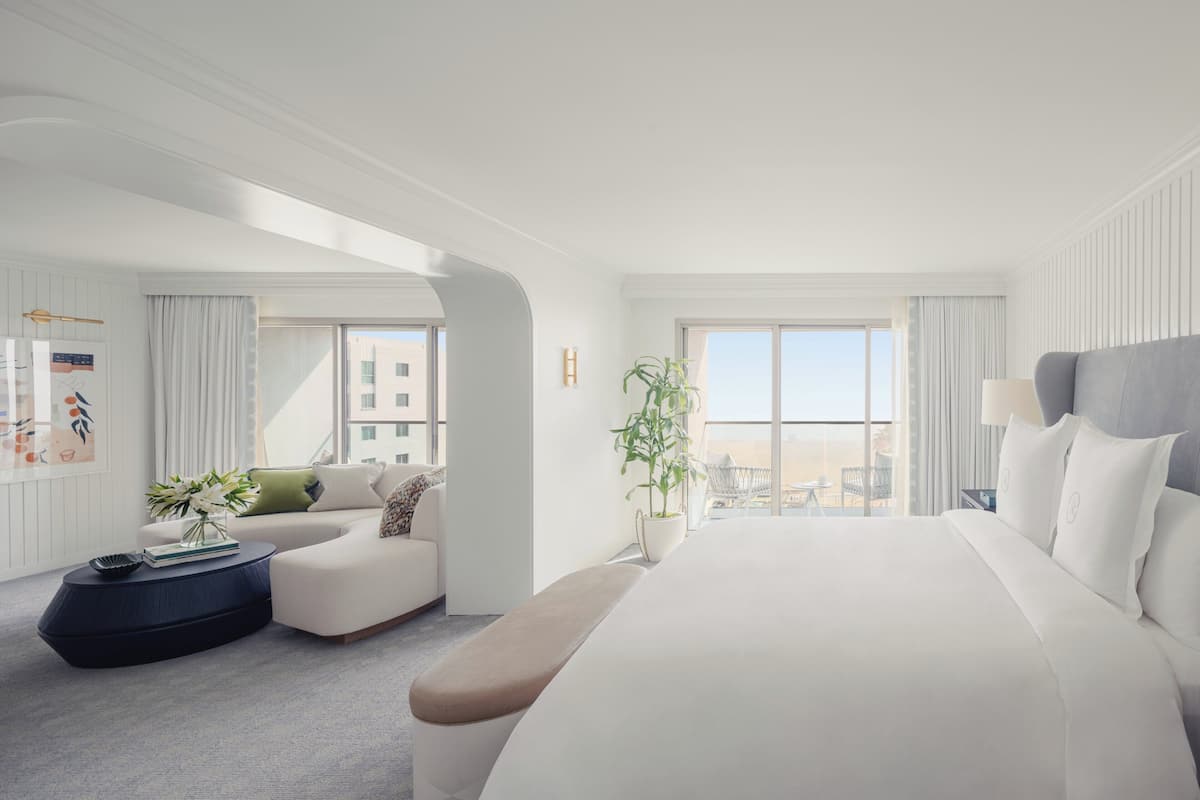 A modern hotel room with a large bed, a sofa, a small table, and a view of the city.